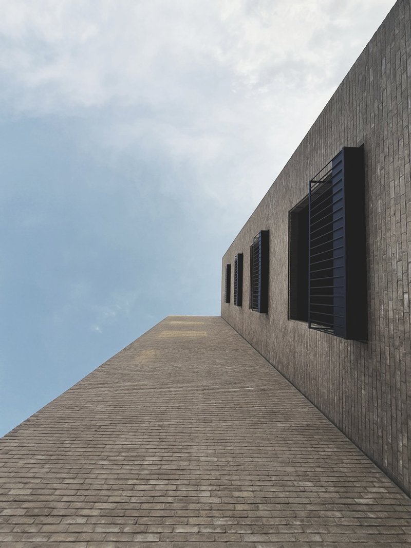 Upward view of the textured brick facade with recessed black shutters against an overcast sky