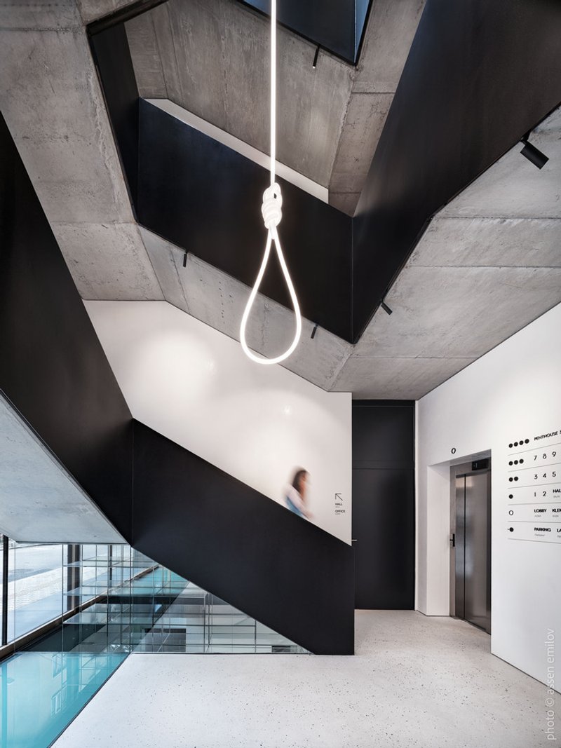 Exposed concrete ceiling above a black folded plate staircase with linear pendant light and person in motion