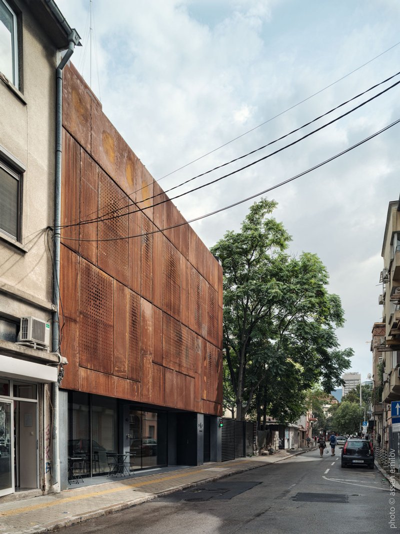 Street elevation showing the full height corten panel facade between neighboring buildings with overhead power lines