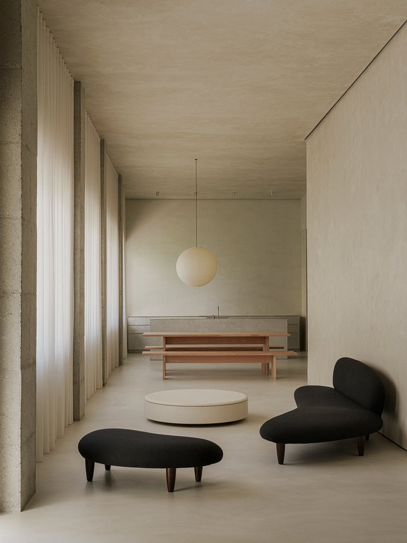 Interior space with concrete columns, sheer curtains, timber benches and black upholstered seating under a sphere pendant