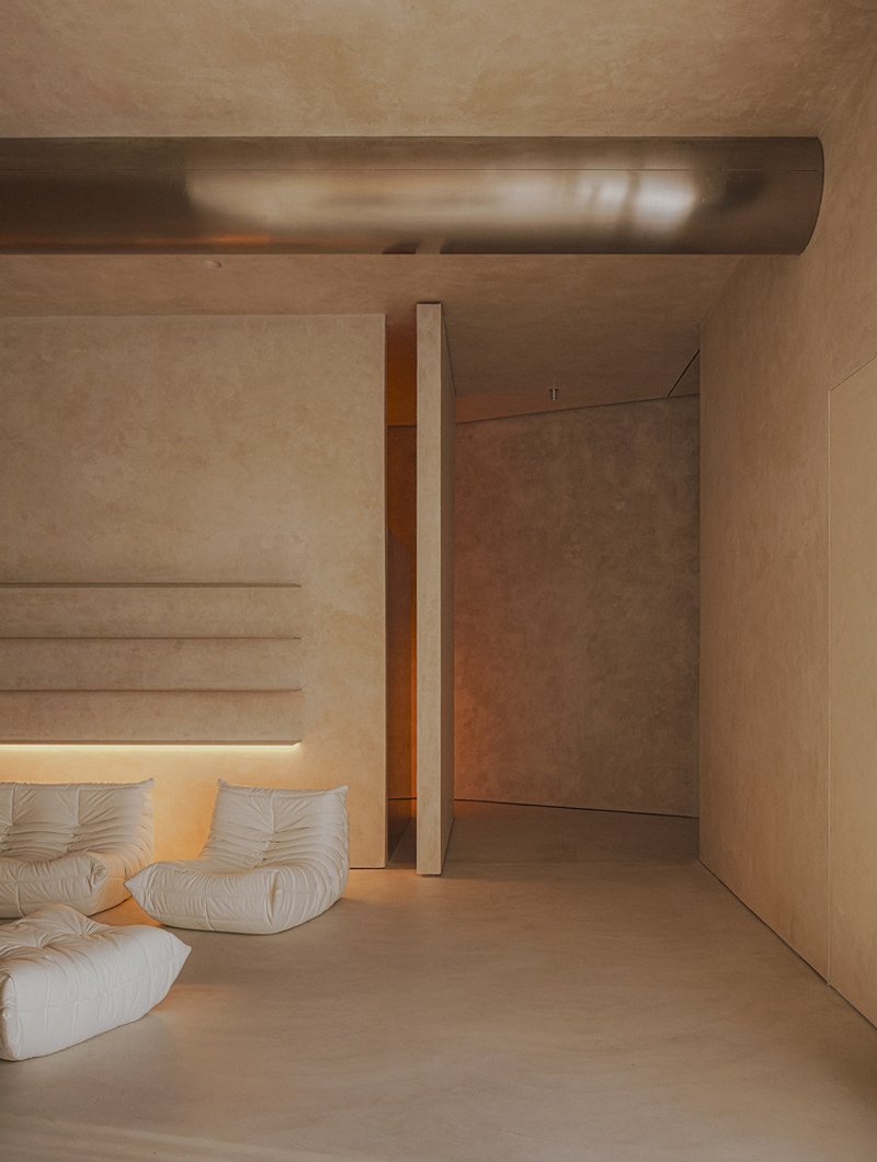 Living area with white upholstered sofa beneath an exposed cylindrical duct and textured plaster walls