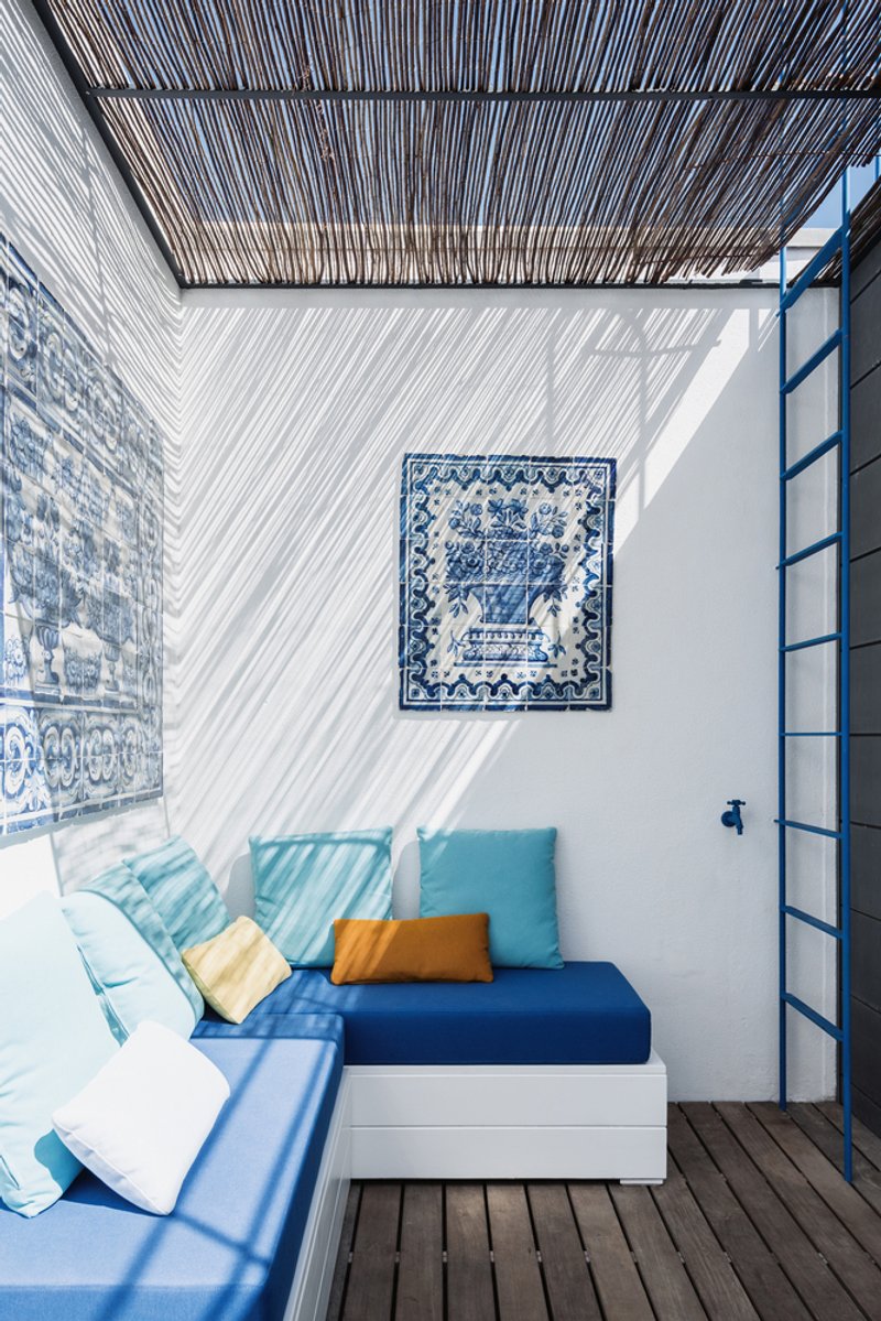 Outdoor seating nook with slatted overhead canopy casting patterned shadows on white walls