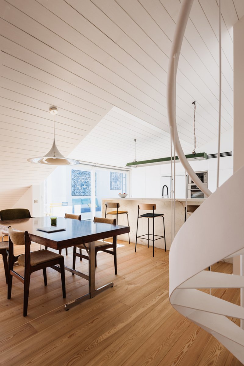 Dining space beneath vaulted wood ceiling with spiral staircase curving into frame