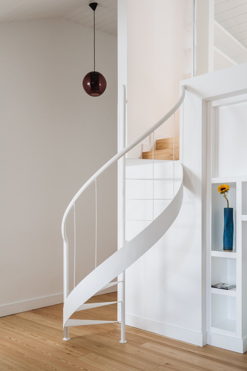 White spiral staircase with vertical balusters and dark red pendant light overhead