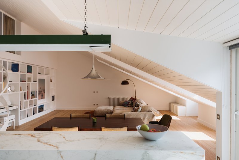 Open-plan living room beneath sloped ceiling with white marble island in foreground and pendant light