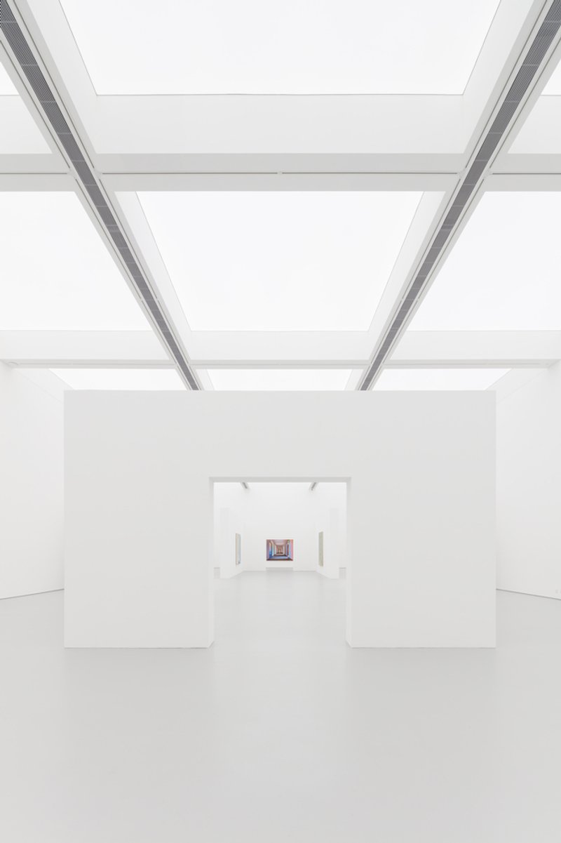Enfilade: deep perspective through aligned white openings, luminous ceiling panels above, a single small painting at the far end