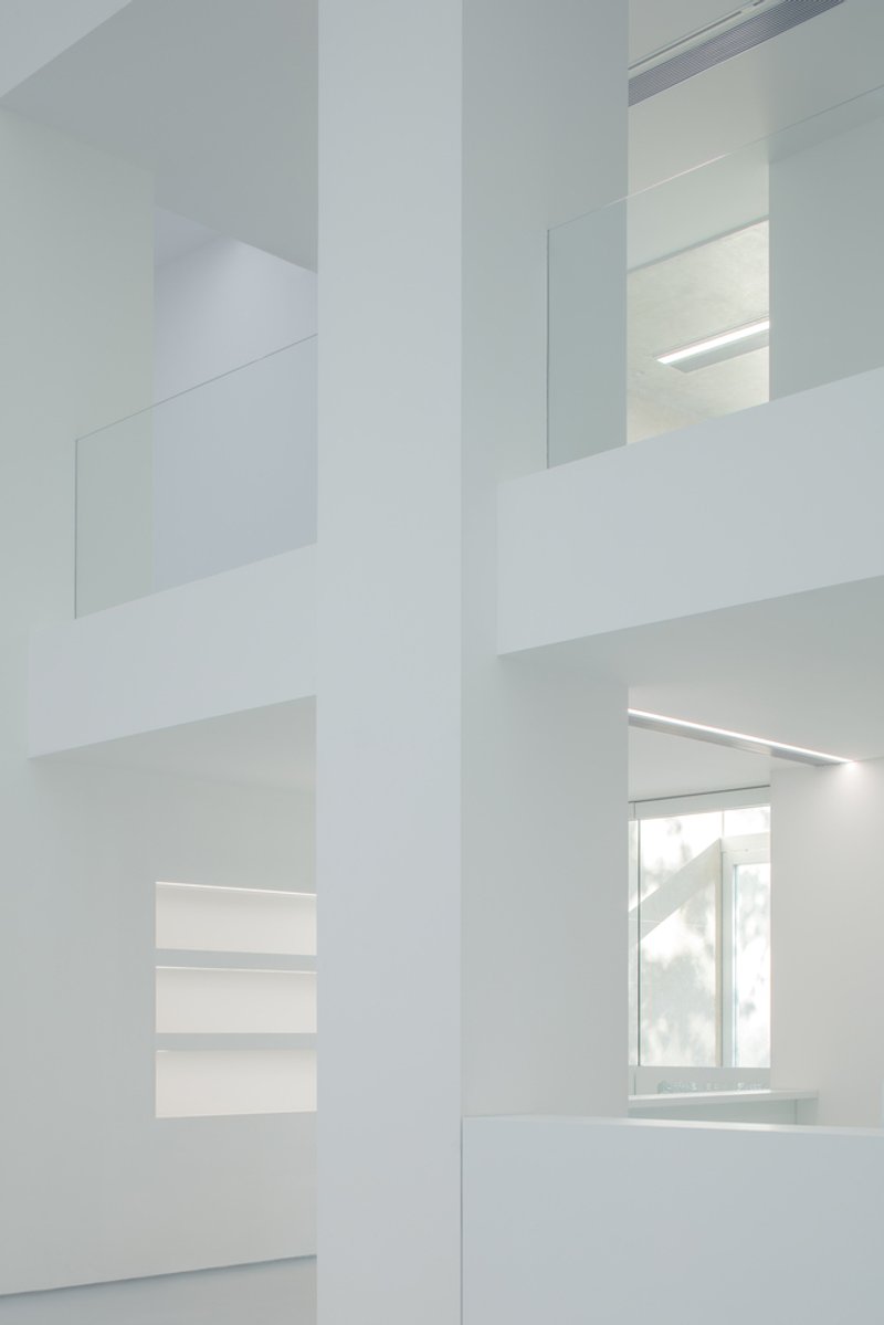 Atrium detail: white walls at multiple levels, glass balustrades, linear lights, window visible through layered openings