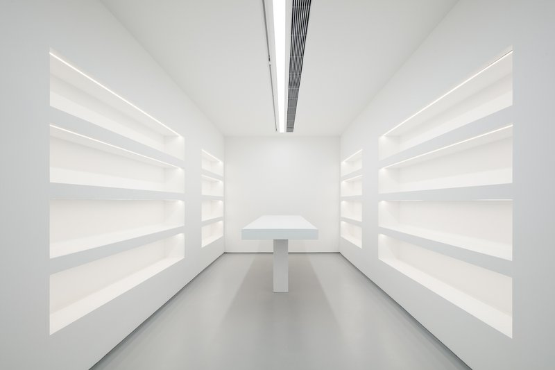 Archive or shop: white shelving on both walls, central display table, linear ceiling light, grey floor