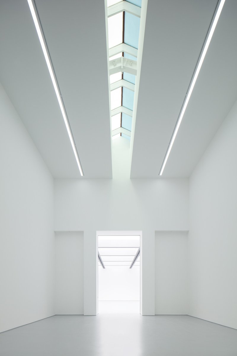 Lobby perspective: skylight strip above, white walls converging toward a bright opening, grey polished floor