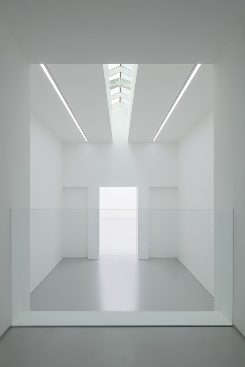 Second-floor void from above: glass balustrade at the edge, white walls, skylight converging above, gallery below
