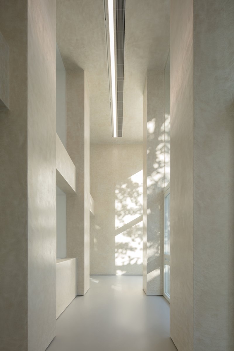 Facade at night: warm light flooding through the three glass openings, white concrete glowing, columns casting shadows