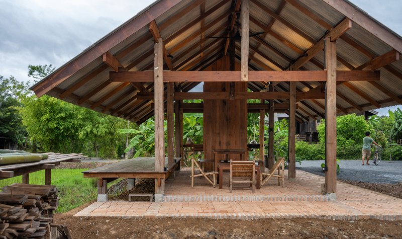 Timber post and beam pavilion with exposed rafters and brick floor with person walking nearby