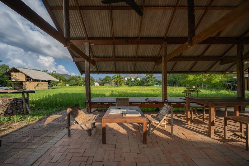 Covered terrace with wooden furniture overlooking green rice paddies under a cloudy sky