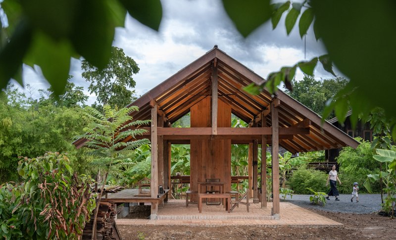 Gabled timber structure with exposed frame and corrugated roof seen through banana trees and garden plantings