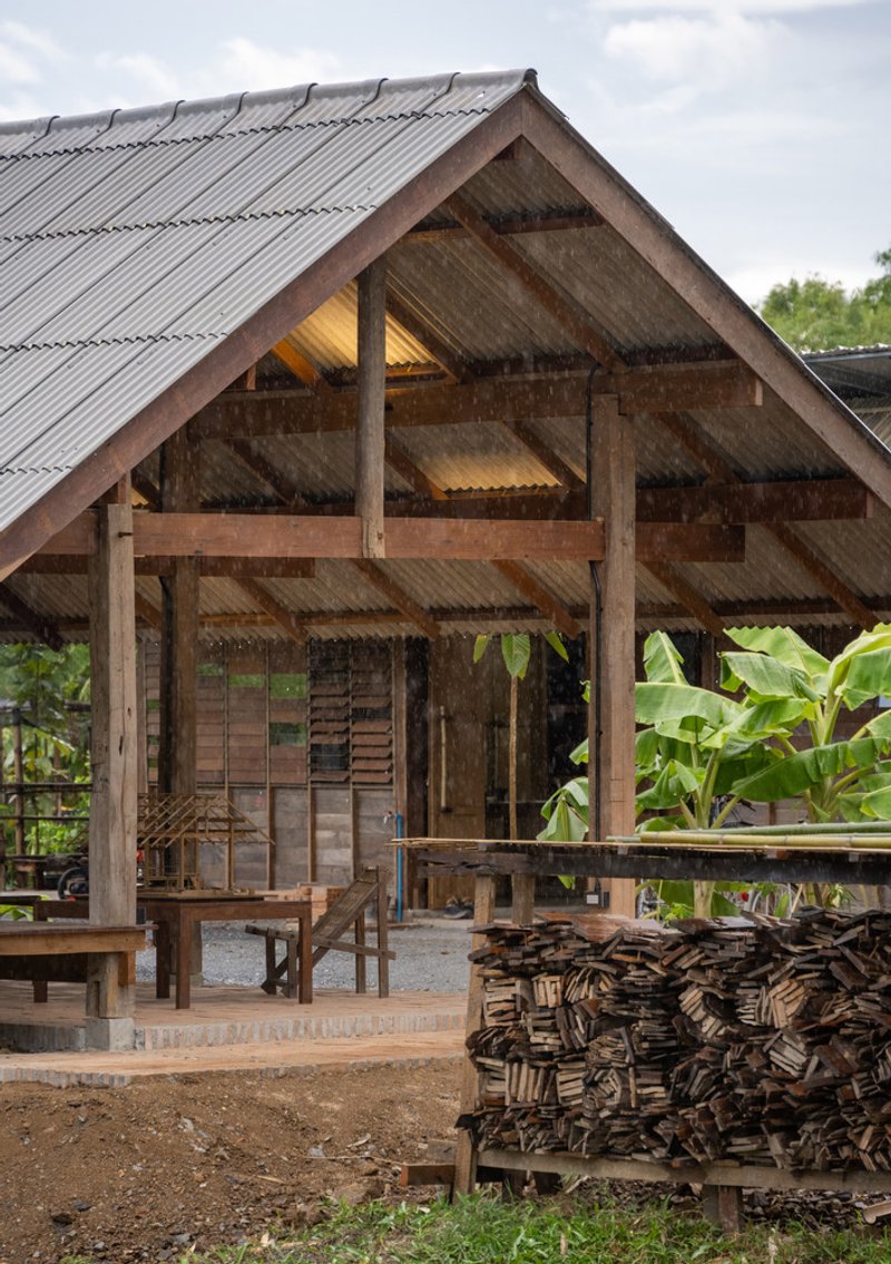 Gable end showing corrugated metal roof, timber framing and stacked firewood beside the open pavilion