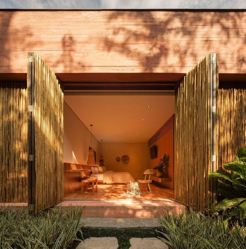 Entry threshold framed by vertical bamboo doors with dappled tree shadows on horizontal timber cladding