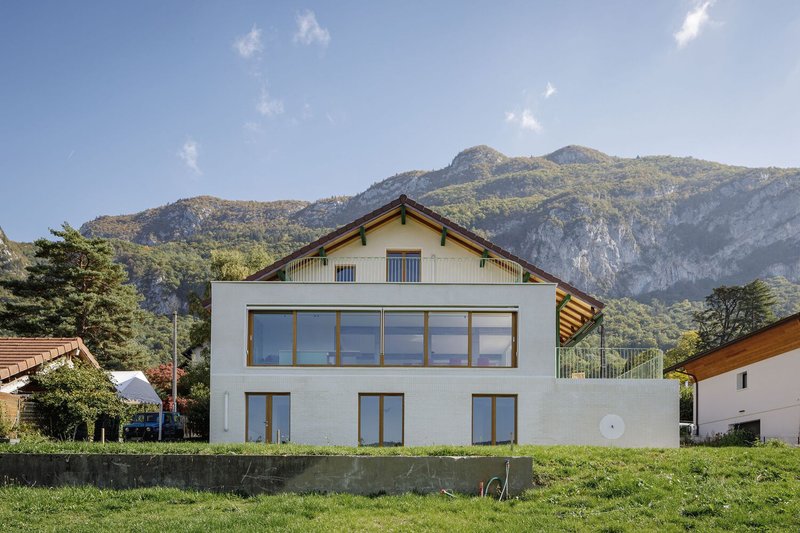 Garden facade: white rendered villa with new ground-floor extension, timber-framed windows, mountains behind