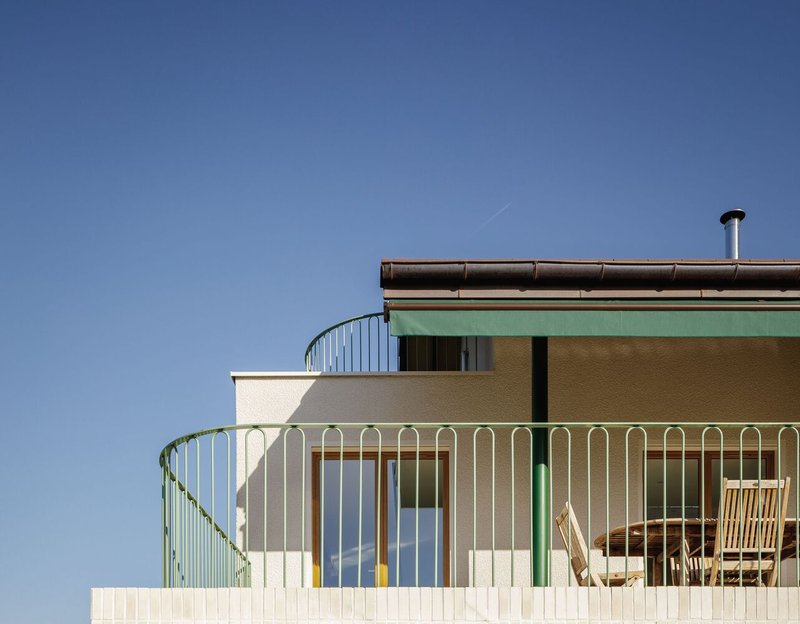 Upper floor detail: green awning, curved metal balcony railing, timber balustrade, blue sky