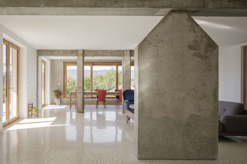 Fireplace wall: house-shaped concrete volume housing the wood stove, terrazzo floor, columns framing the view