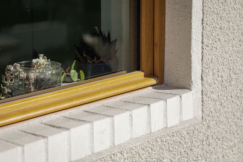 Window sill detail: white brick sawtooth course, oak timber frame, rendered wall texture
