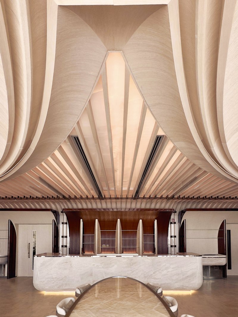 Ilios upper floor: folded ceiling forms converging to a peak above the marble bar, white chairs