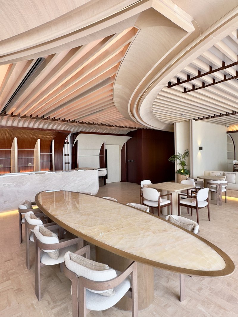 Ilios dining: curved timber ceiling sweeping over an oval table, white upholstered chairs