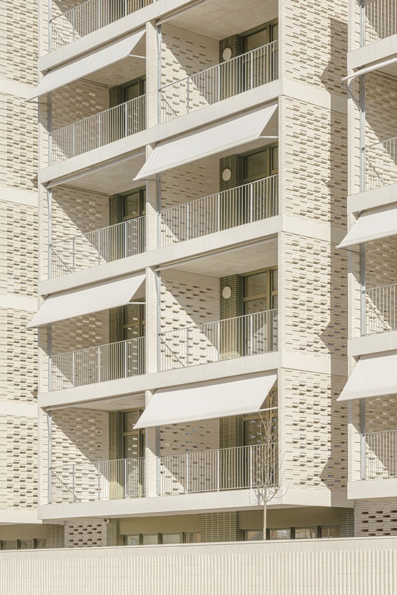 Balcony detail: folding triangular awnings on each balcony, cream brick piers, ceramic brise-soleil panels between windows