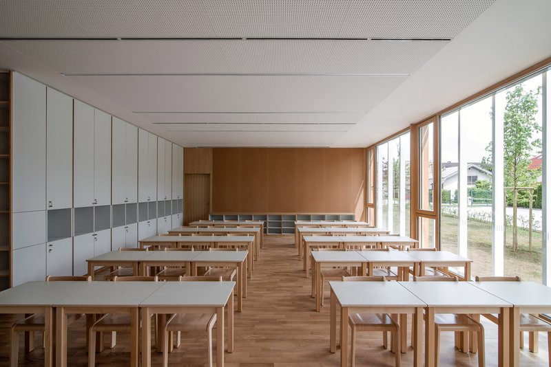 Classroom: timber desks and chairs, cork rear wall, white storage cabinets, full-height windows with garden view