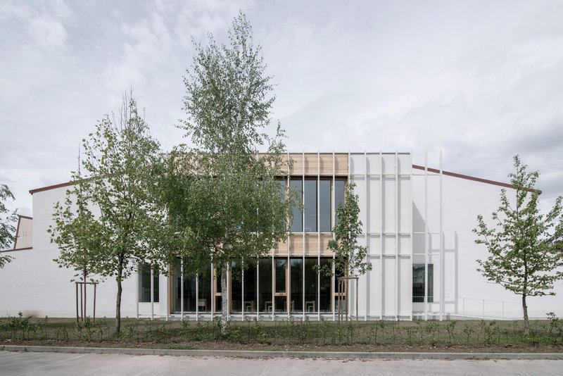 East facade: white vertical metal fins, timber-clad upper storey with full-height glazing, birch trees, overcast sky