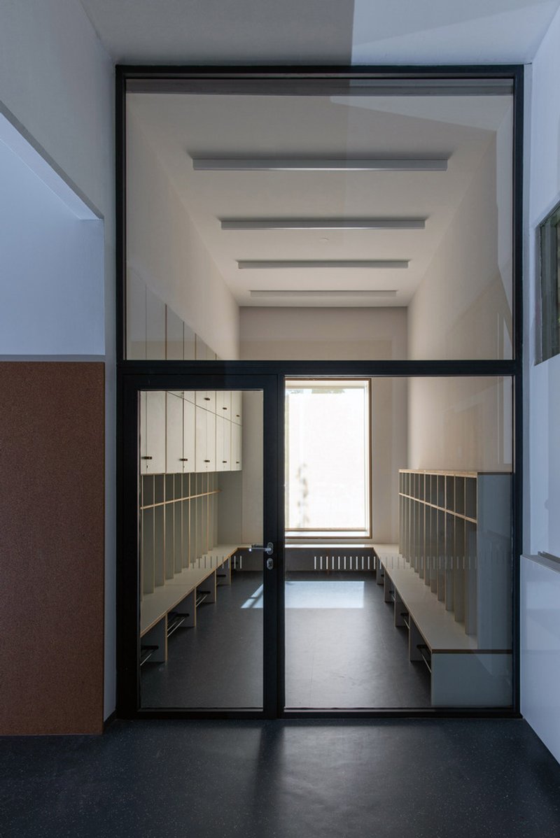 Changing room entrance: glass door, grey lockers and cubbies visible inside, cork accent wall panel