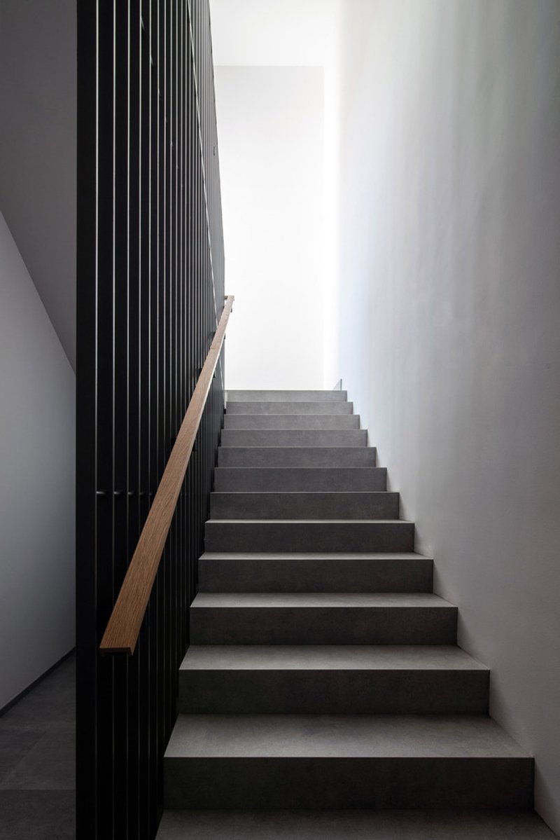 Staircase: dark concrete steps, black metal slatted screen, timber handrail, light from above