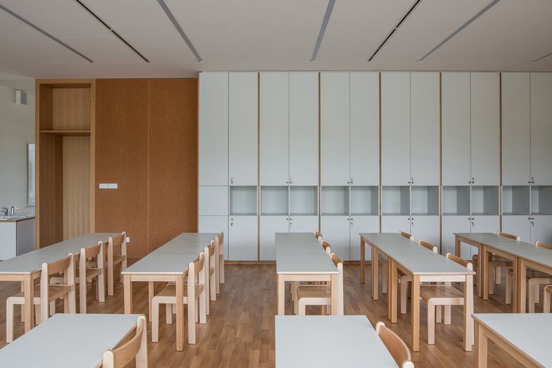Classroom: rows of timber desks, white lockers along the wall, cork panel, pendant lights, clean and bright