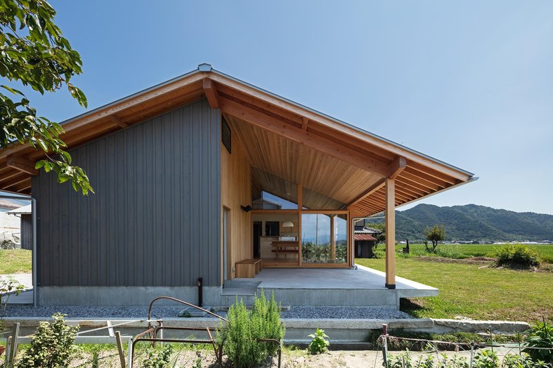 Entry side: pitched roof with deep cedar-lined overhang, metal cladding, concrete step, garden, mountains in background