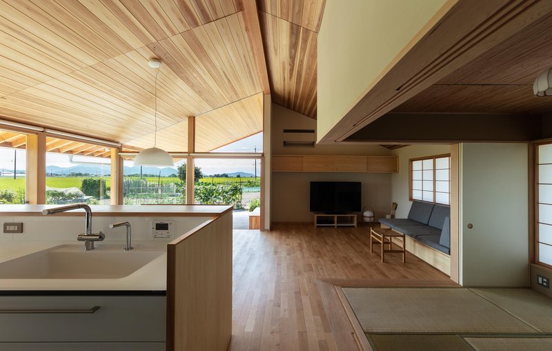 Kitchen and living: cedar ceiling rising to ridge, open-plan kitchen island, sofa, TV unit, tatami room with blue sliding doors beyond