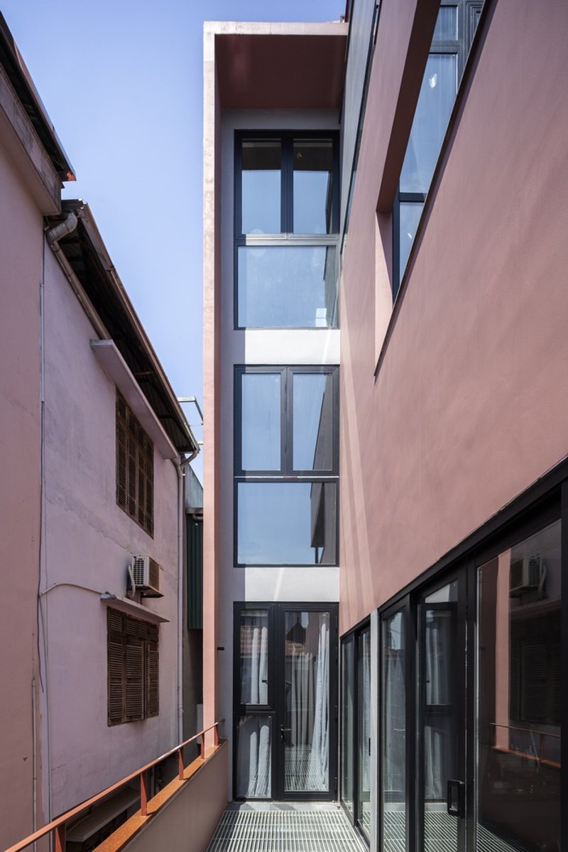 Narrow courtyard framed by pink stucco walls with a stacked glass volume rising between them