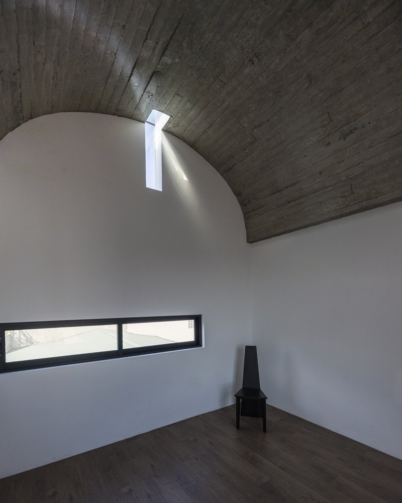Vaulted ceiling room with board-formed concrete and a narrow skylight casting daylight down white walls