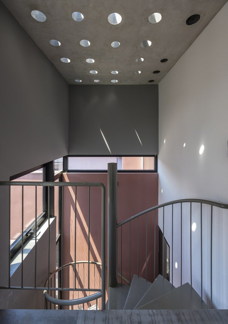 Spiral staircase beneath a concrete ceiling pierced with circular skylights filtering afternoon sun