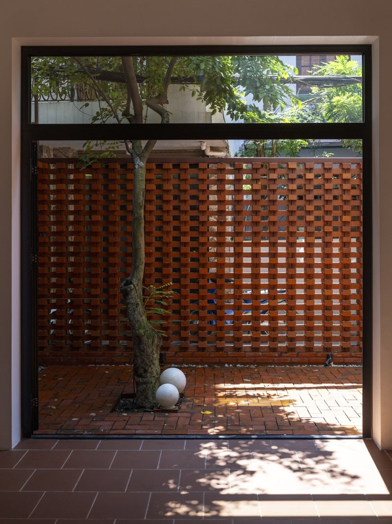 View through doorway to brick courtyard with young tree and perforated screen wall in dappled sunlight