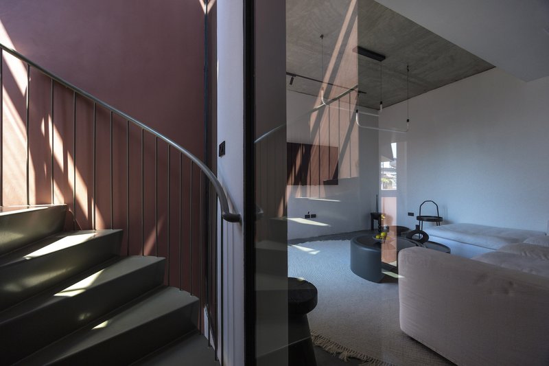 Open-plan living space with curved kitchen island and spiral staircase under an exposed concrete ceiling
