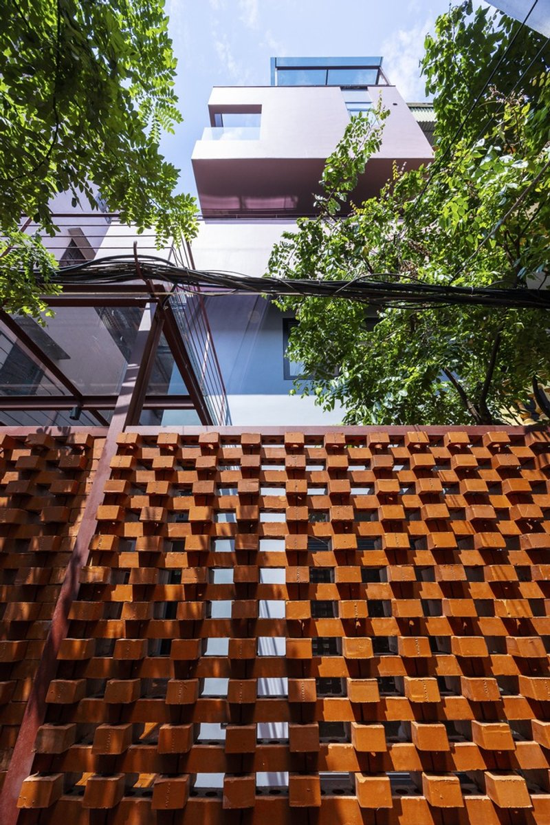 Upward view of chequered terracotta brick screen wall framed by green foliage and overhead power lines