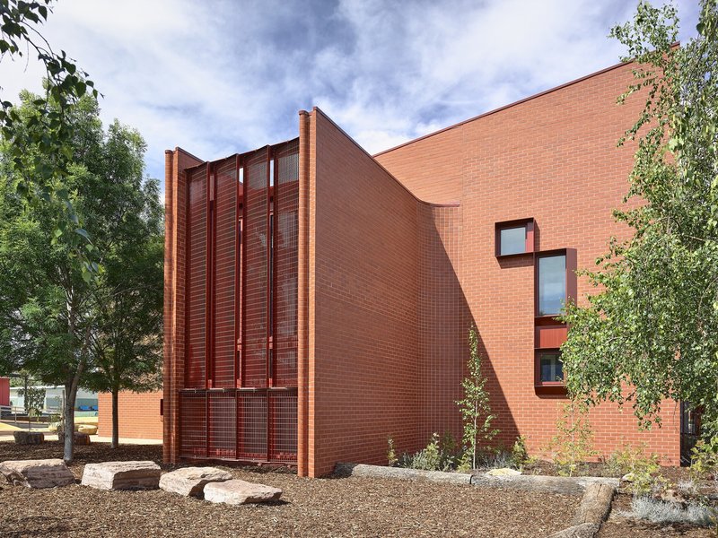 Curved brick wall with angled roofline and vertical metal louver screen flanked by trees