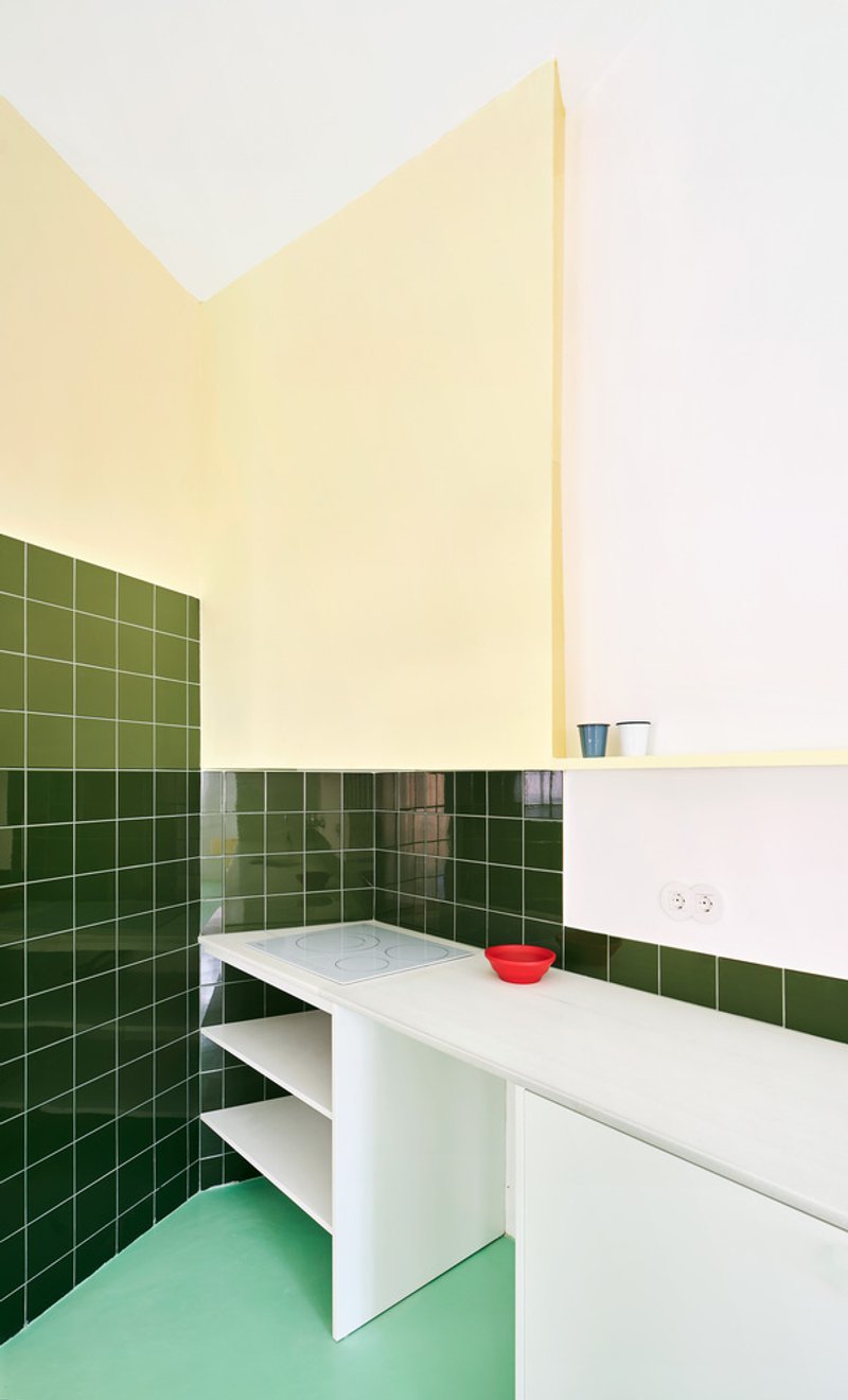 Kitchen corner showing dark green tile walls, white counter with red bowl, and pale green flooring