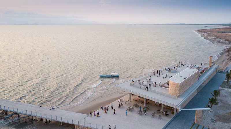 Rooftop terrace and beach plaza filled with visitors at dusk beside still coastal waters