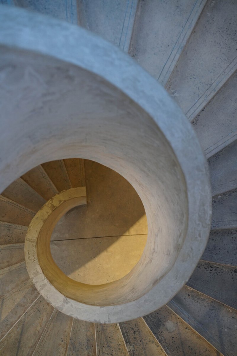 Top-down view of spiral concrete staircase with warm light illuminating the curved center void