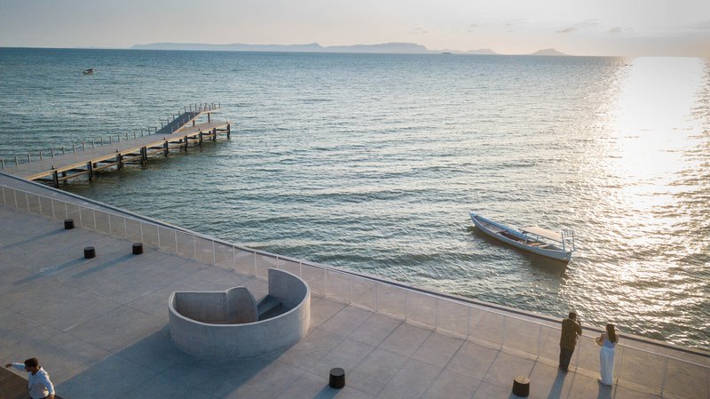 Curved concrete seating element on the terrace plaza with visitors at sunset near the water's edge