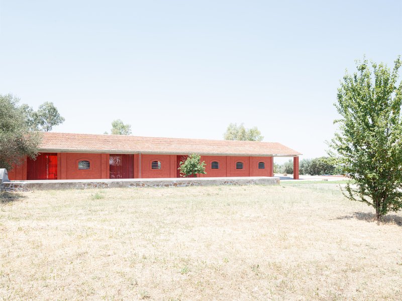 Red brick facade with tiled roof and louvered vents set in a dry summer landscape