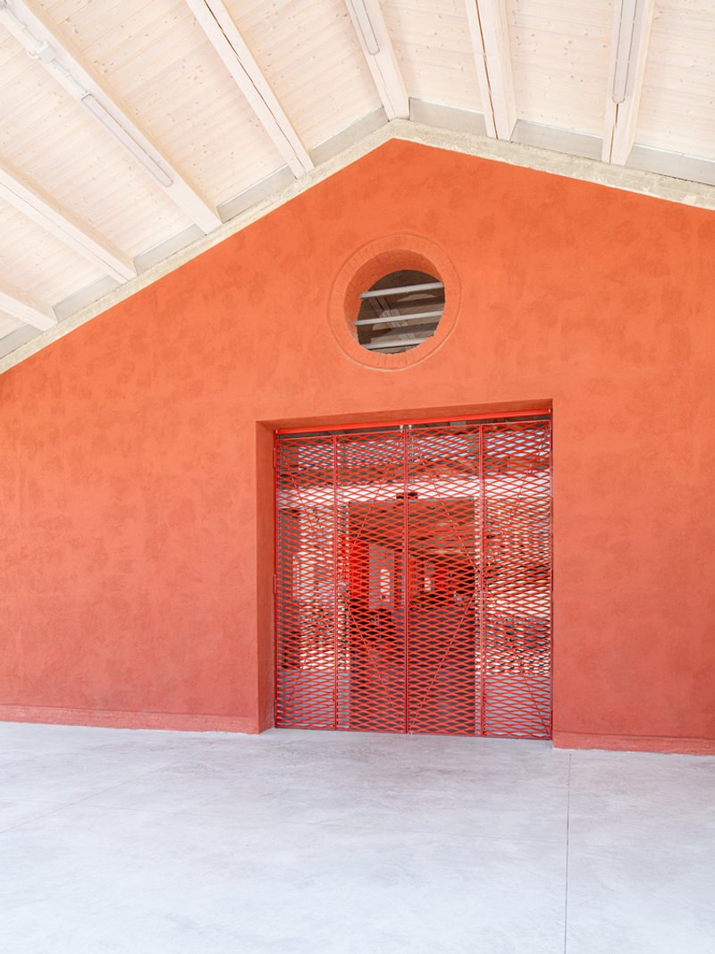 Orange stucco facade with red mesh gate and circular window beneath a white timber ceiling