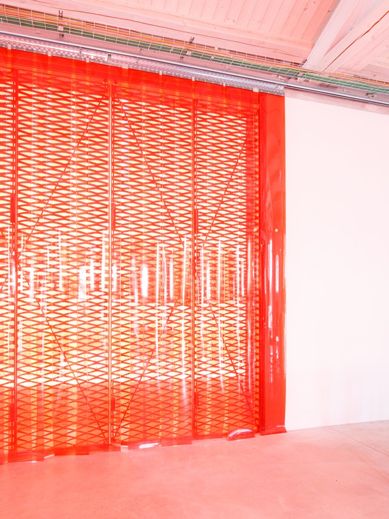 Red perforated metal screen partially opened to reveal an interior courtyard bathed in light