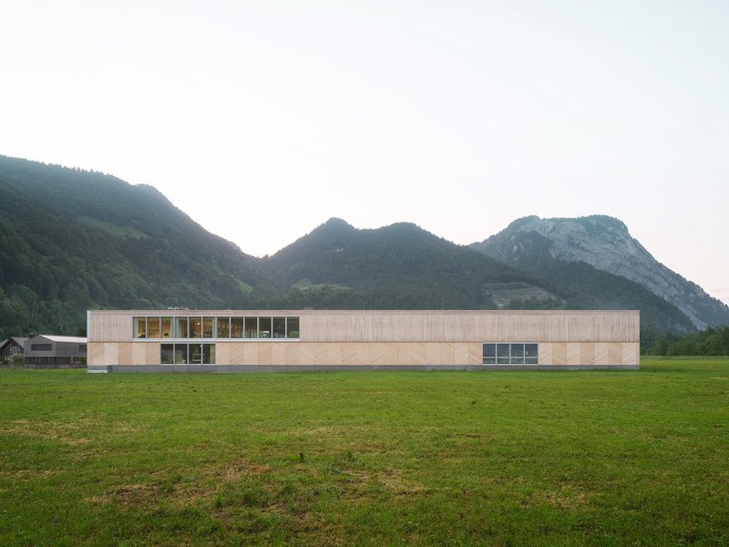 Linear facade with timber cladding and ribbons of glazing stretching across an open meadow at dusk