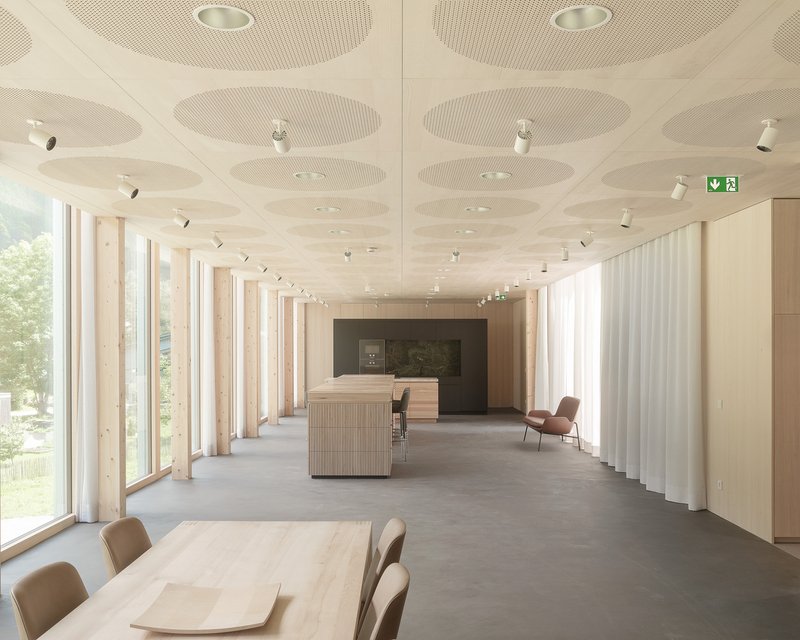 Reception space with perforated acoustic ceiling panels, timber columns, white curtains and a polished concrete floor